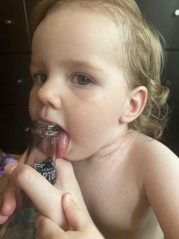 Toddler mouths beer bottle rim alongside Cartel beer close-ups