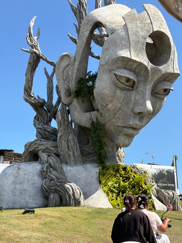 Weathered stone face sculpture emerges from tangled roots in Kediri