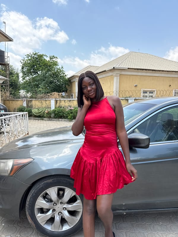 Woman poses in red dress beside car in Abuja