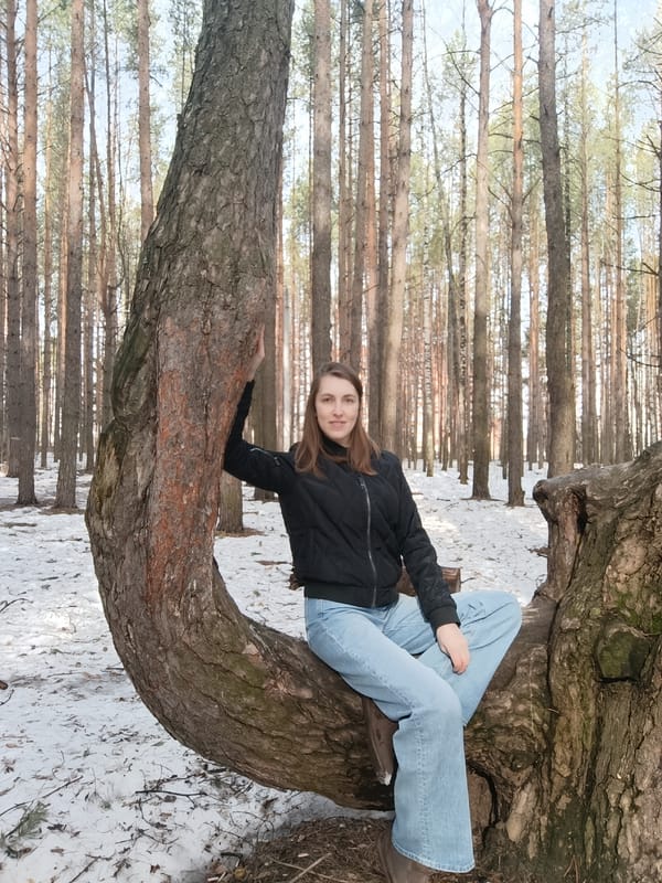 Woman sits on curved tree trunk in forest