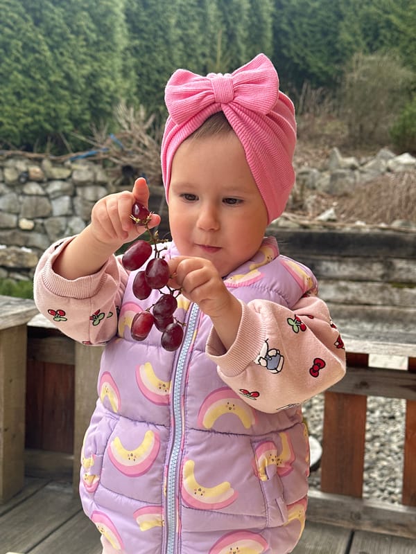 Baby in colorful winter outfit holds grapes in Wisła