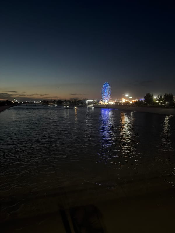 Blue-lit Ferris wheel glows on a Nukus waterfront pier at night