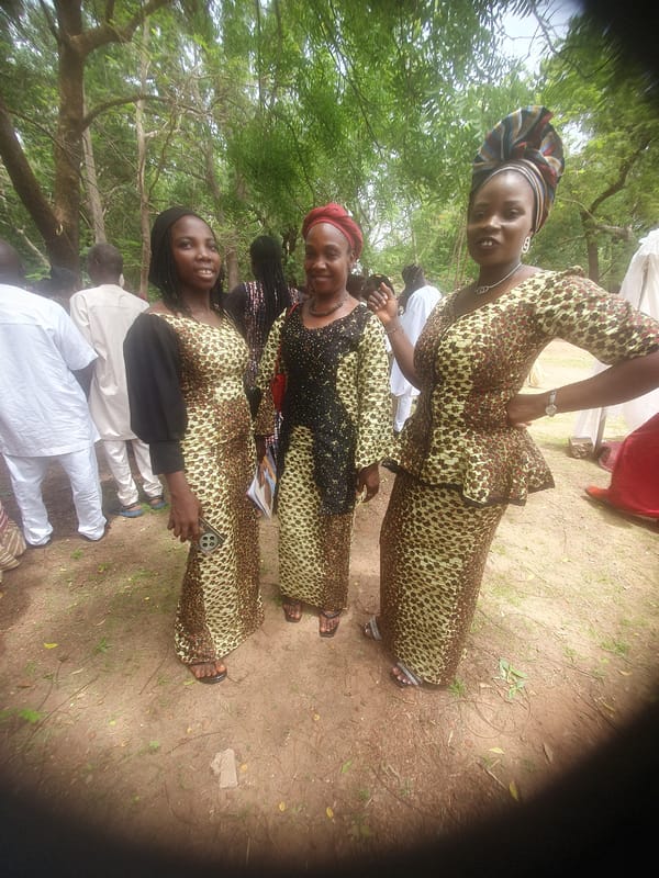 Three women in matching dresses gather in grassy area