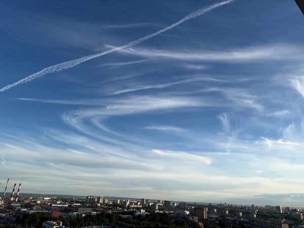 City skyline under open blue skies with contrails overhead