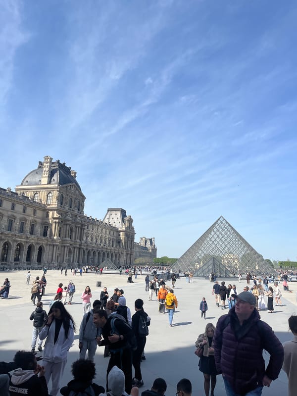 Crowds gather at Louvre Museum plaza under clear skies