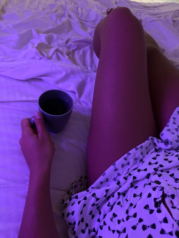 Purple-lit bedroom evening with coffee and rumpled white sheets