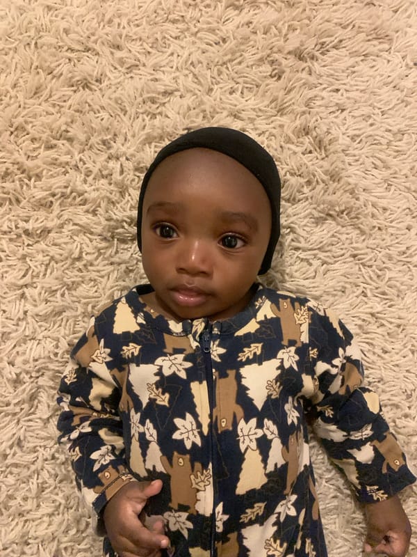 Baby in patterned outfit photographed on rug in Nigeria