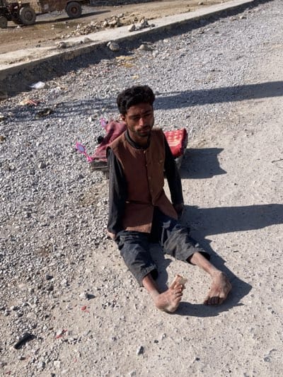 Person sits barefoot on gravel road in Quetta