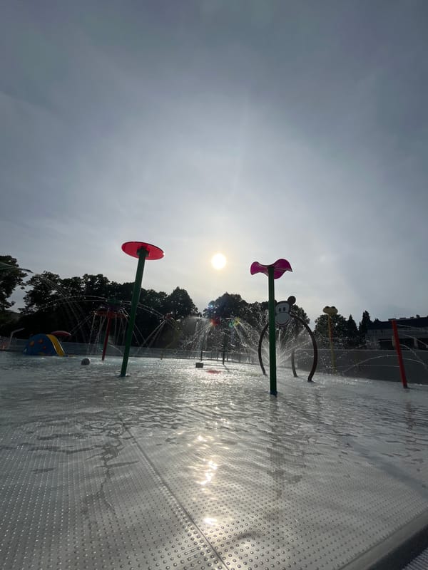 Outdoor pool and splash pad facility documented under varied sky