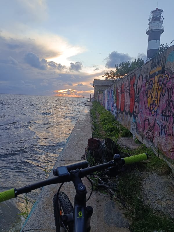 Striped lighthouse and bicycle at the water's edge, sunset