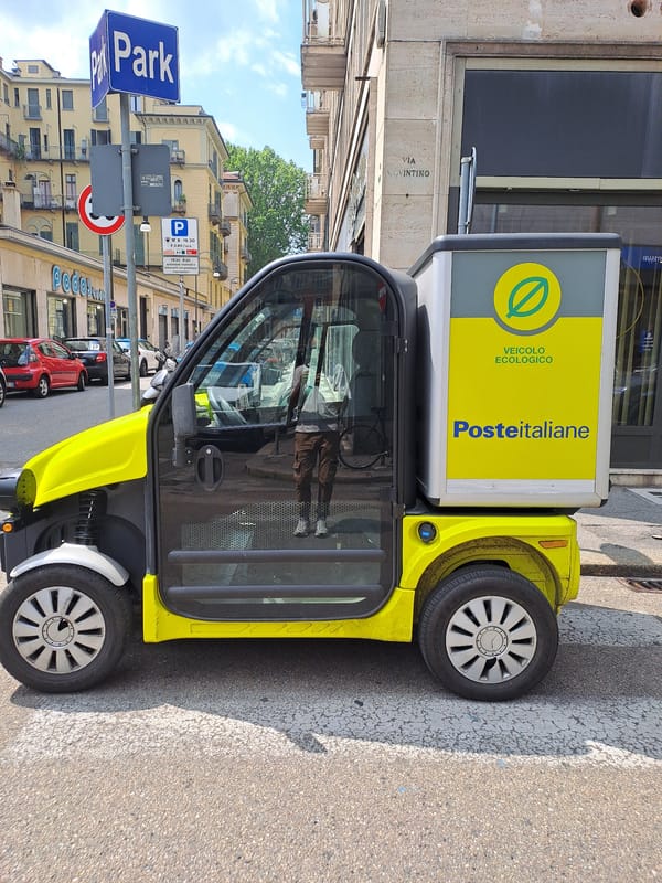 Electric postal van and Vespas parked on a Turin street