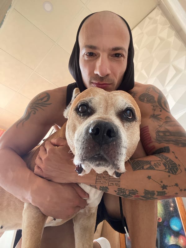Tattooed arms wrapped around a light brown dog indoors