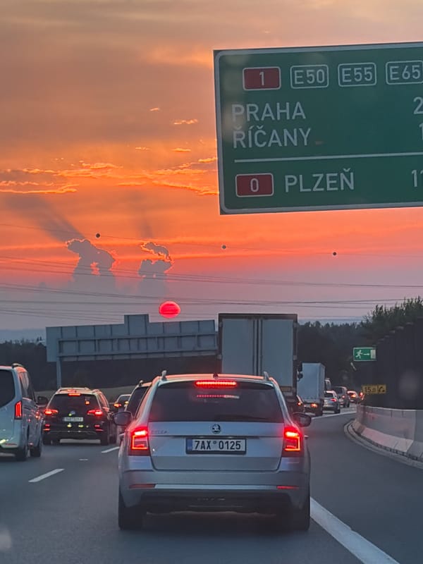 Rush hour traffic rolls through suburban Prague under a sunset sky