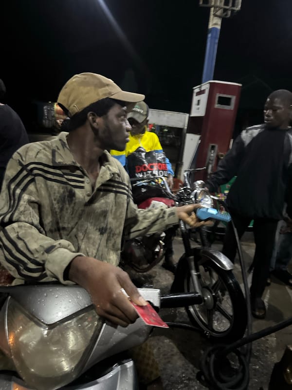 Man with red card sits on motorcycle at Nigerian gas station