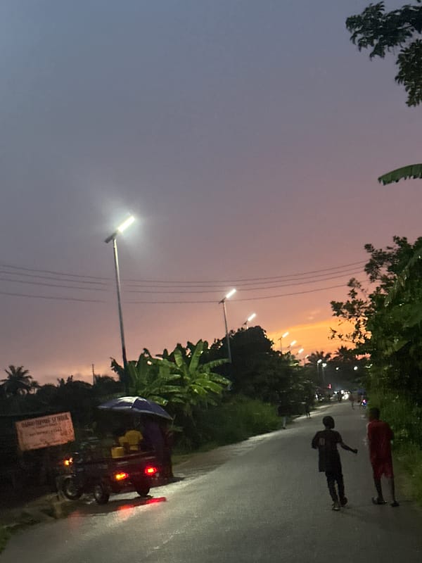 Two pedestrians walk roadside during dusk in Ikot Ekpene