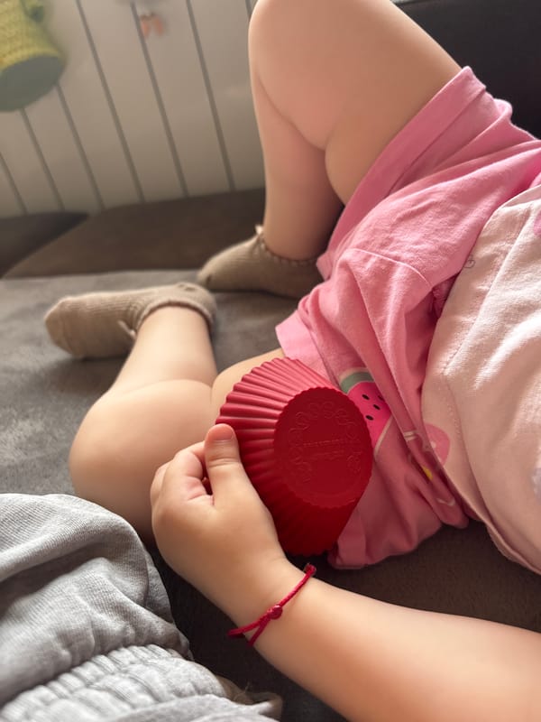 Child with red bracelet and silver ring plays with cupcake liner
