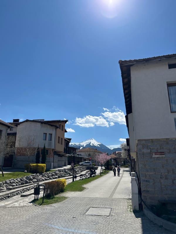Pedestrians stroll through sunny Bansko with mountain backdrop