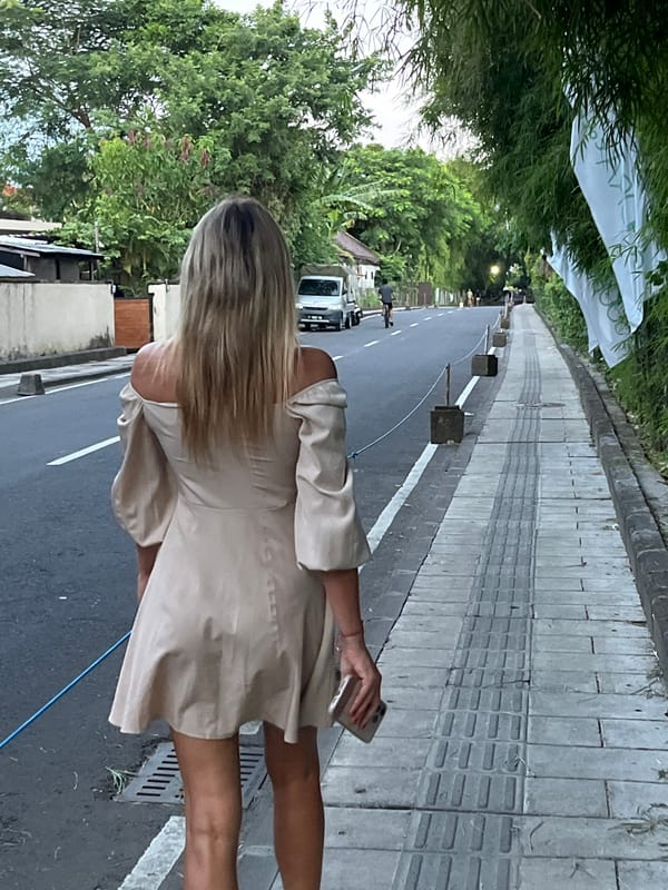 Woman walks Indonesian street amid tropical greenery, passing truck