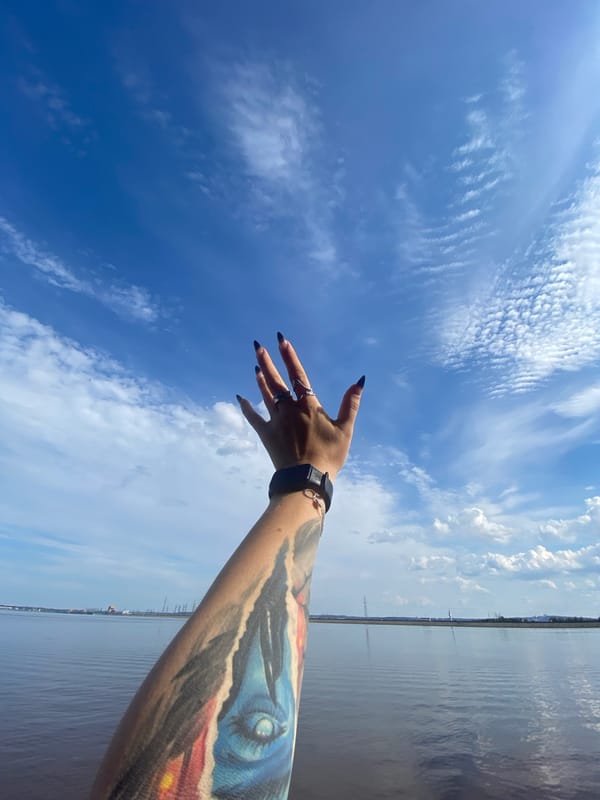 Tattooed arm reaching skyward against blue summer sky