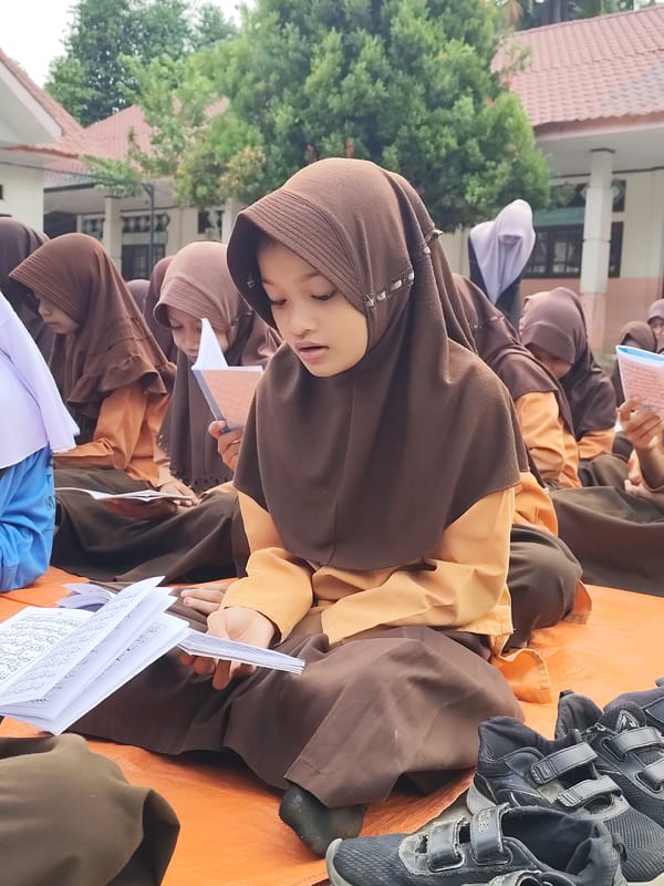 Students gather outdoors for organized reading session on orange tarp