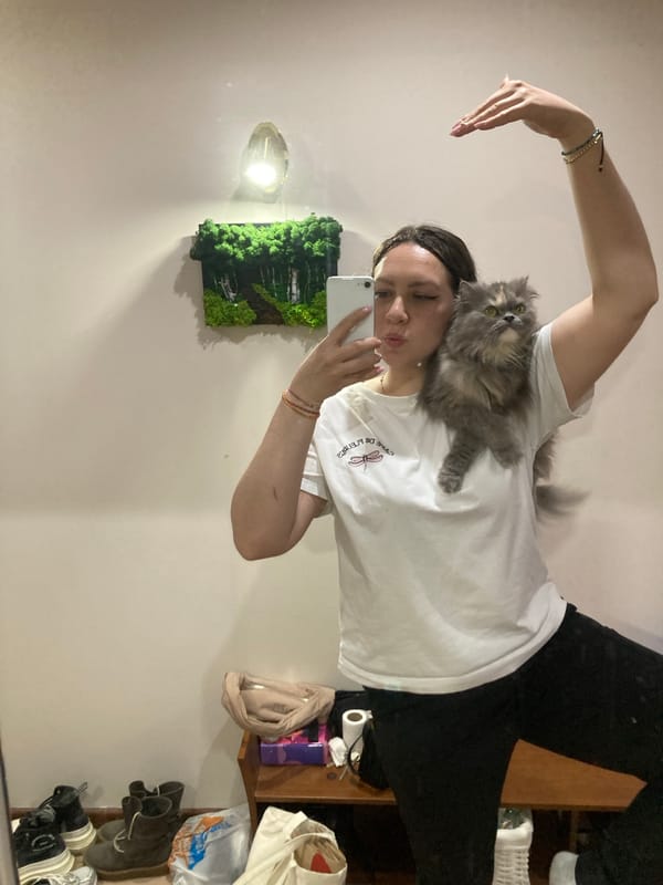 Woman takes selfie with gray cat on shoulder indoors